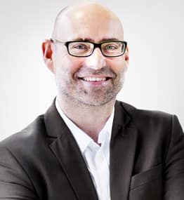 A man in glasses and a suit smiling for the camera.