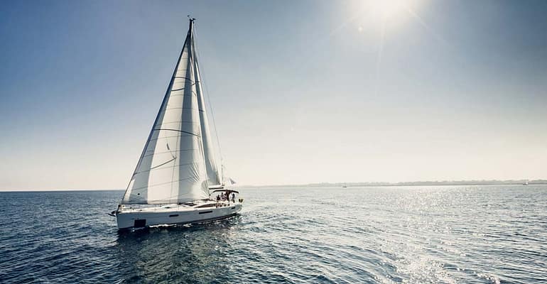 A sail boat sailing on the ocean under a blue sky.