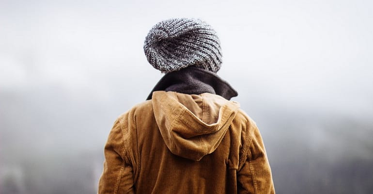 A person wearing a jacket and hat standing in the snow.